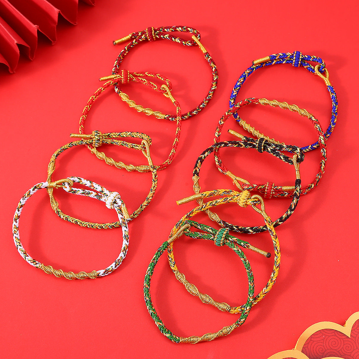 Collection of colorful braided rope bracelets with gold-tone knots on a red background