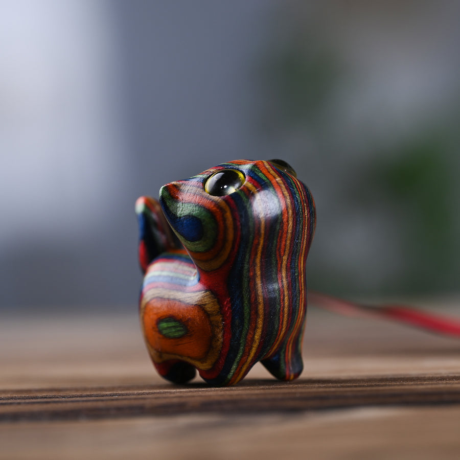 Close up of a small rainbow wood cat carving with a bell on a red string