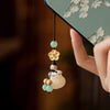 Close up of a wooden money bag charm with a yellow flower bead hanging from a phone