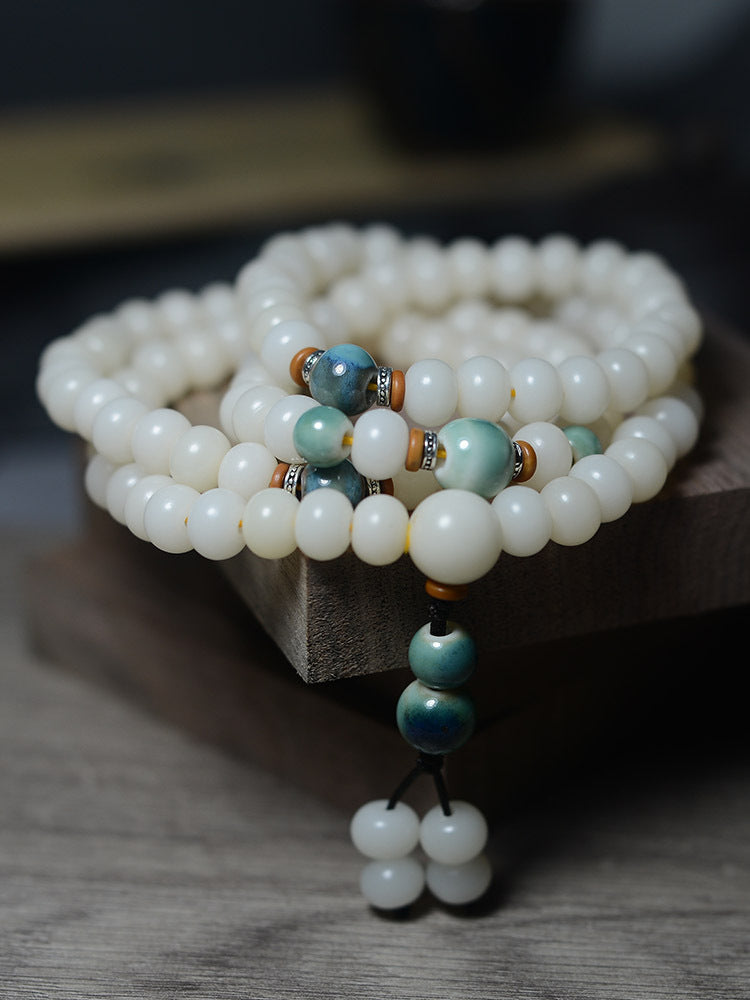 Coiled white bodhi seed mala bracelet with blue accent beads on wood