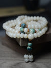 Coiled white bodhi seed mala bracelet with blue accent beads on wood