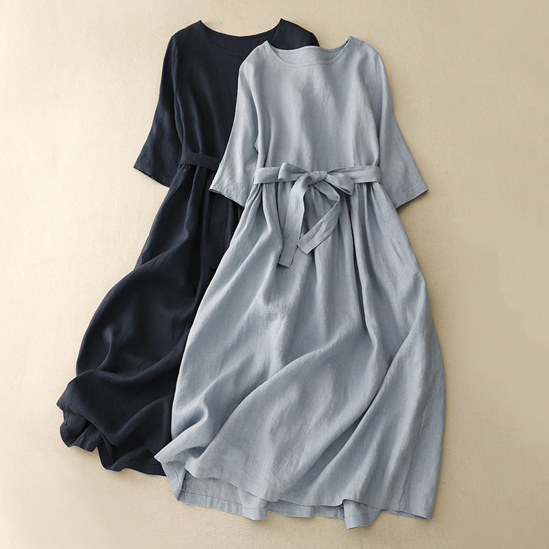 Light blue and navy blue short sleeve midi dresses with tie belts lying on a beige surface