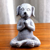 A grey textured statue of a dog sitting in a meditation pose with paws together