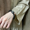 A wrist wearing a black silver sheen obsidian bracelet with a carved grey lion charm.