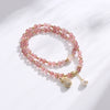 Double wrap bracelet with pink strawberry quartz beads and a gold money bag charm on a white background