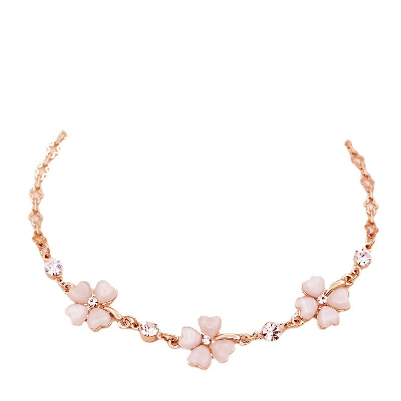 Close-up of a rose gold bracelet with pink crystal four-leaf clover charms on a purple background