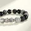 Close up of a beaded bracelet with a silver Pixiu charm and black and grey stones