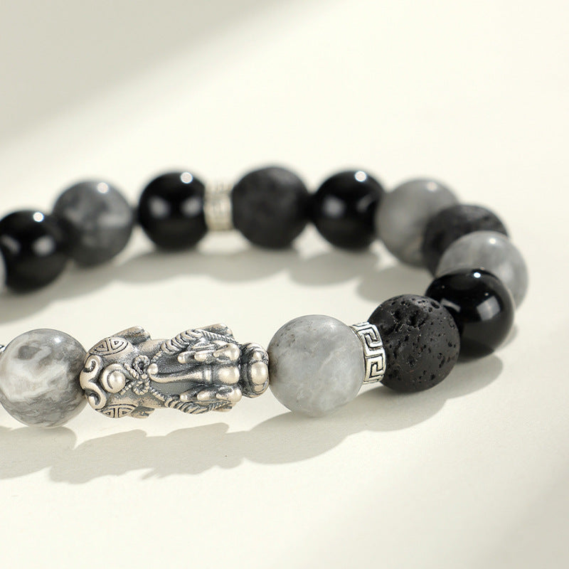 Close up of a beaded bracelet with a silver Pixiu charm and black and grey stones