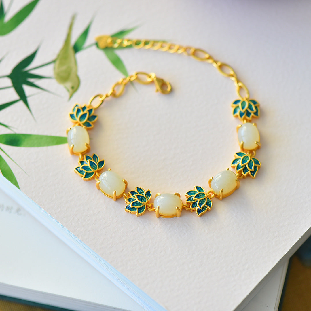 Gold-tone bracelet with white jade stones and green enamel lotus leaves on a book