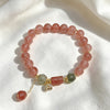 Pink strawberry quartz bracelet with grey moonstone beads and a gold flower charm on a mirror surface