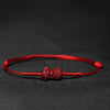 A red woven cord bracelet with a carved red cinnabar charm in the center