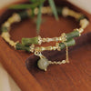 Close up of green bamboo bead bracelet with gold links and agate drop on wooden tray