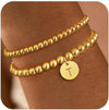 Two gold-tone beaded bracelets worn on a wrist, one with a letter T charm