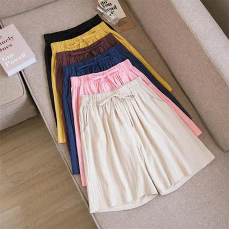 A stack of colorful cotton linen shorts with drawstring waists on a beige sofa