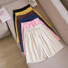 A stack of colorful cotton linen shorts with drawstring waists on a beige sofa