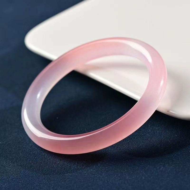 A translucent pink stone bangle bracelet resting on a white surface