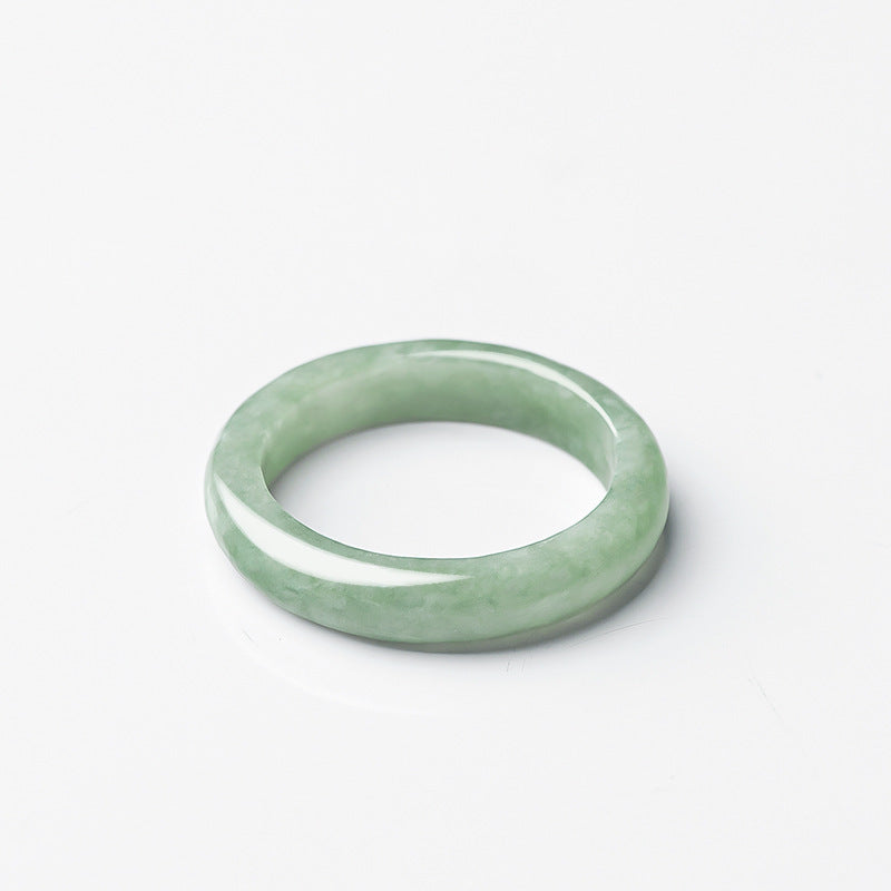 Close up view of a polished light green jade ring on a white background