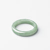 Close up view of a polished light green jade ring on a white background