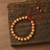 Close up of a sandalwood bead bracelet with a red cord on a wooden surface