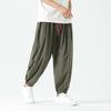 Man wearing olive green loose harem pants with red drawstrings and white sneakers