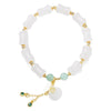 Close-up of a white jade bracelet with bamboo-shaped beads and a hanging lucky bag charm on a wooden surface