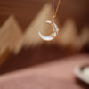 Close up of a white mother-of-pearl crescent moon pendant on a gold chain