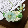 Pink glass lotus flower in a small green bowl with white stones on a wooden table