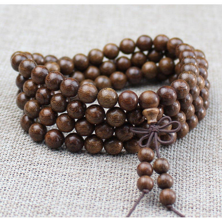 Close-up of a brown wooden 108 bead mala bracelet coiled on a textured surface