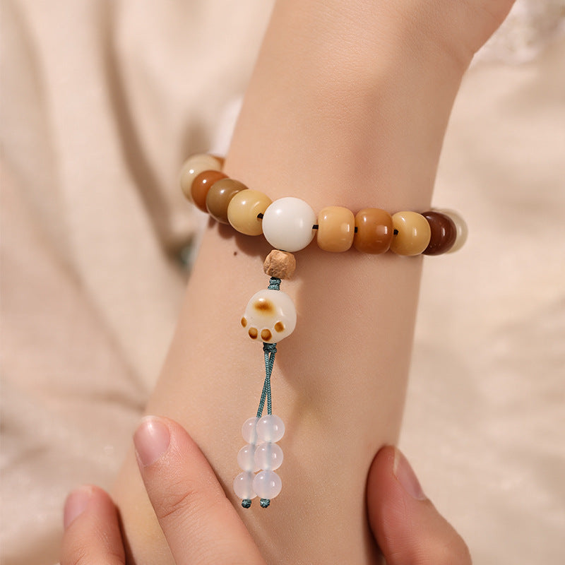 Close up of a wrist wearing a caramel colored bodhi seed bracelet with a white charm pendant.