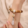 Close up of a wrist wearing a caramel colored bodhi seed bracelet with a white charm pendant.