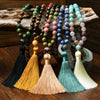 Five long stone bead necklaces with colorful tassels resting on a wooden surface