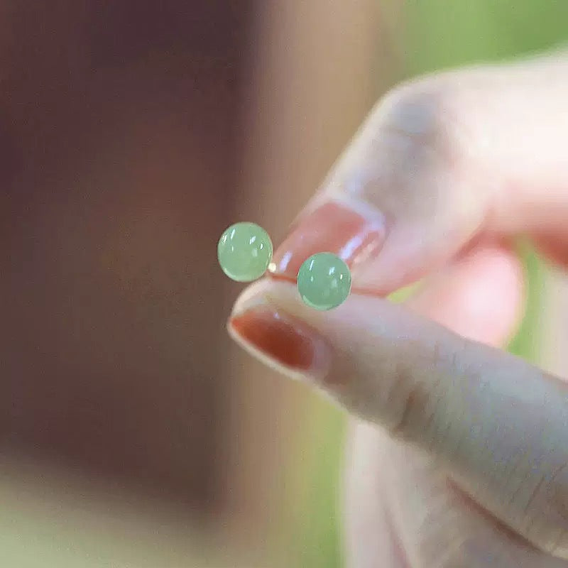 Close up of small green round beaded stud earrings held between fingers