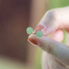 Close up of small green round beaded stud earrings held between fingers