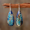 Pair of blue teardrop Emperor Stone earrings hanging on a wooden branch