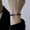 Close-up of a black woven bracelet with a silver-tone Nine-Eye Dzi pattern charm on a wrist