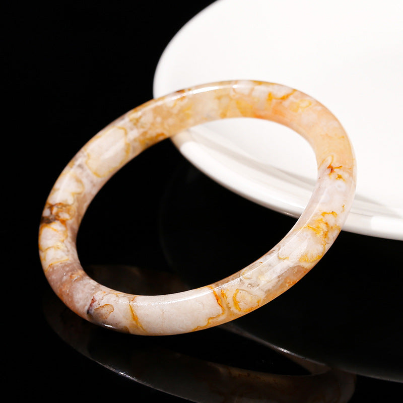 A polished natural crystal bangle bracelet with orange and white patterns resting on a black surface