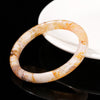 A polished natural crystal bangle bracelet with orange and white patterns resting on a black surface