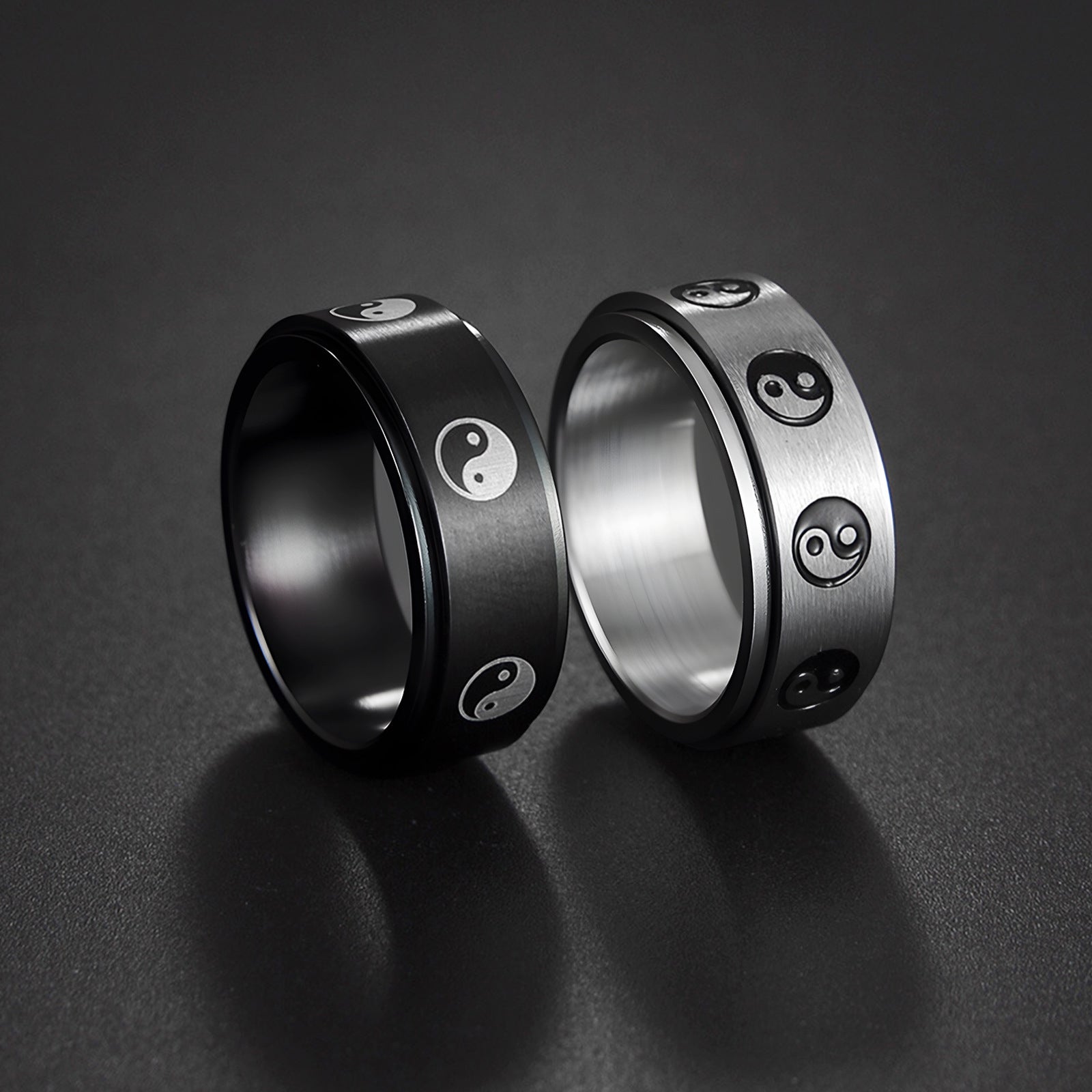 Black and silver stainless steel rings with rotating Yin Yang symbols on a dark background