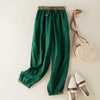 Green cotton linen harem pants with elastic waist laid flat next to accessories