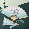 Open Chinese style folding fan with lotus print and bamboo ribs resting on a dark surface