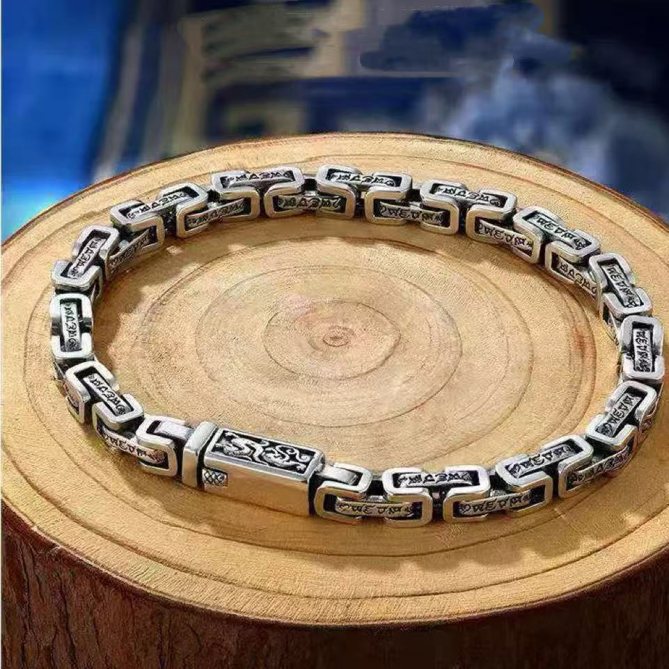 Silver-tone copper chain bracelet with dragon engravings resting on a wooden slice