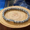 Silver-tone copper chain bracelet with dragon engravings resting on a wooden slice