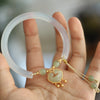 Hand holding a translucent white chalcedony bangle with a gold-tone Ruyi lock charm and green beads