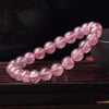 A close-up of a pink strawberry quartz beaded bracelet on a dark wooden surface