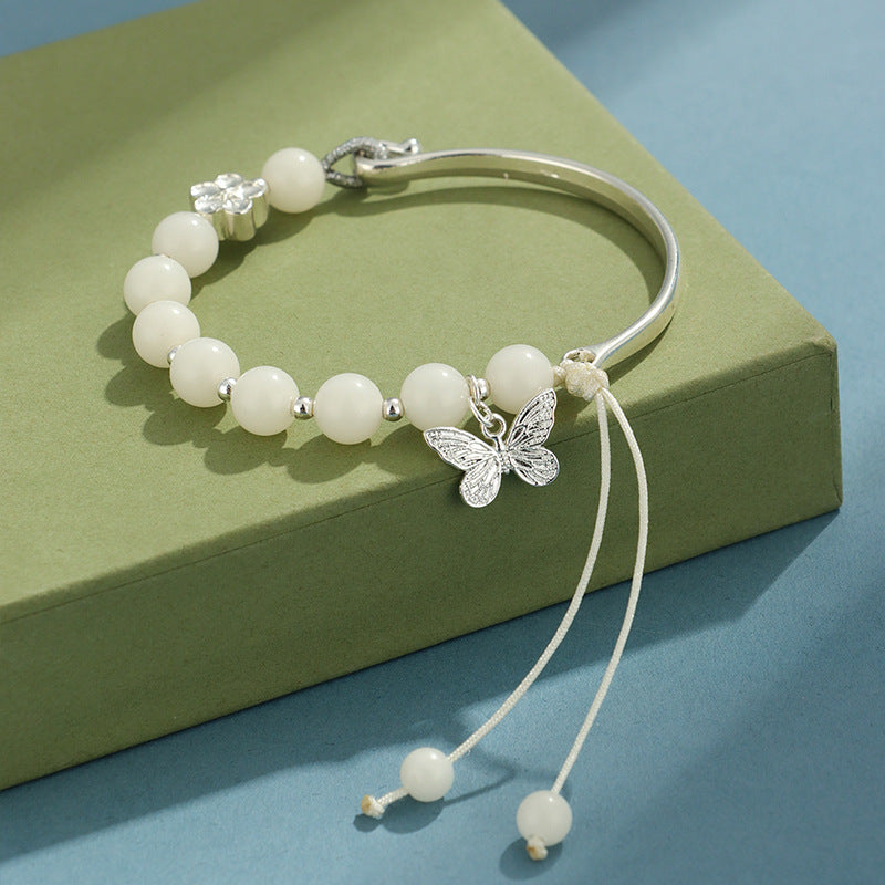 Silver tone cuff bracelet with white bodhi beads and a butterfly charm on a green box