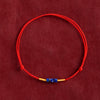 A close-up of a red woven cord bracelet with small blue stone beads and gold accents on a red background