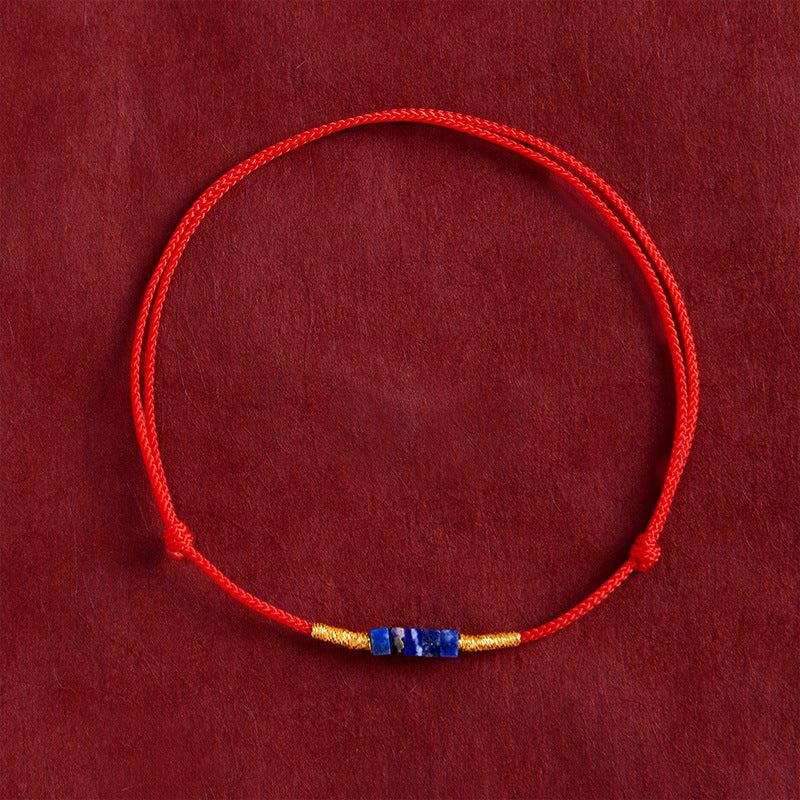 A close-up of a red woven cord bracelet with small blue stone beads and gold accents on a red background