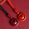 Two red cinnabar pendants on black and orange cords lying on a textured surface