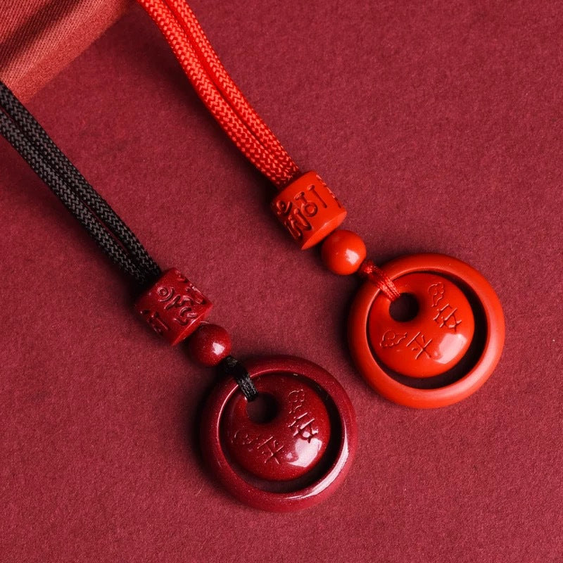 Two red cinnabar pendants on black and orange cords lying on a textured surface
