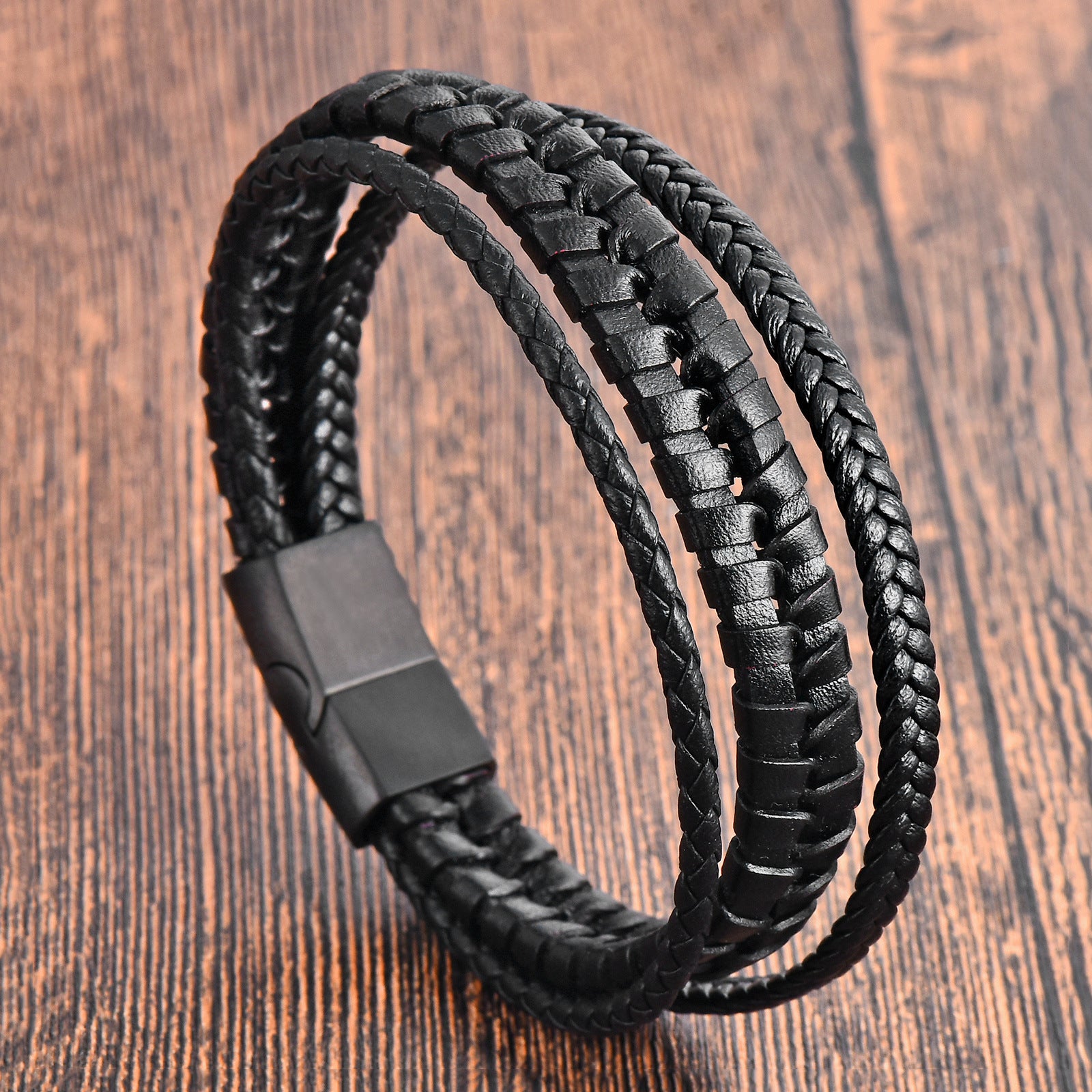 Close up view of a black braided leather bracelet with a rectangular metal clasp on a wooden surface
